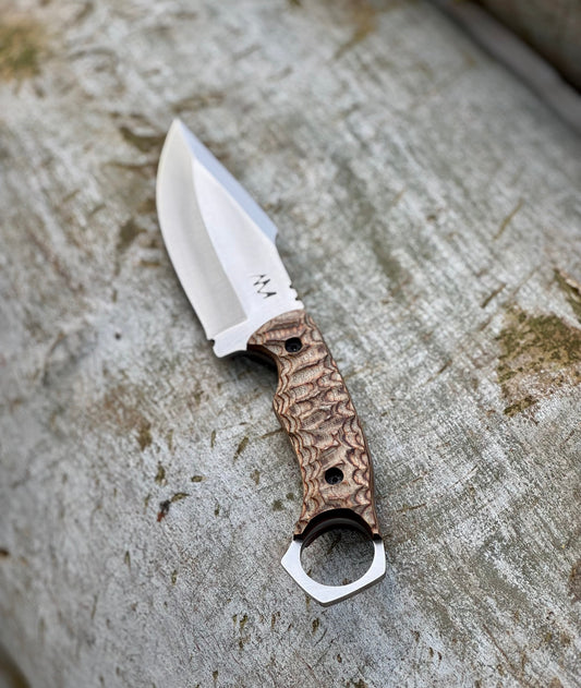 Close-up of G10, wood, and bone knife handles arranged on a log outdoors