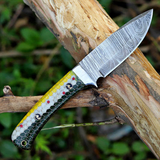 Hand-forged Damascus fixed blade knife with honeycomb resin handle displayed outdoors.