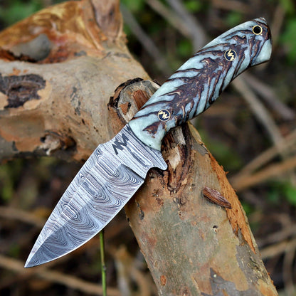 AM Shard Damascus knife displayed on rugged outdoor surface showcasing pine cone resin handle and patterned steel blade.